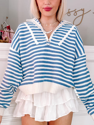 Blue and white striped knit pullover with half-zip closure, paired with a white ruffled skirt.
