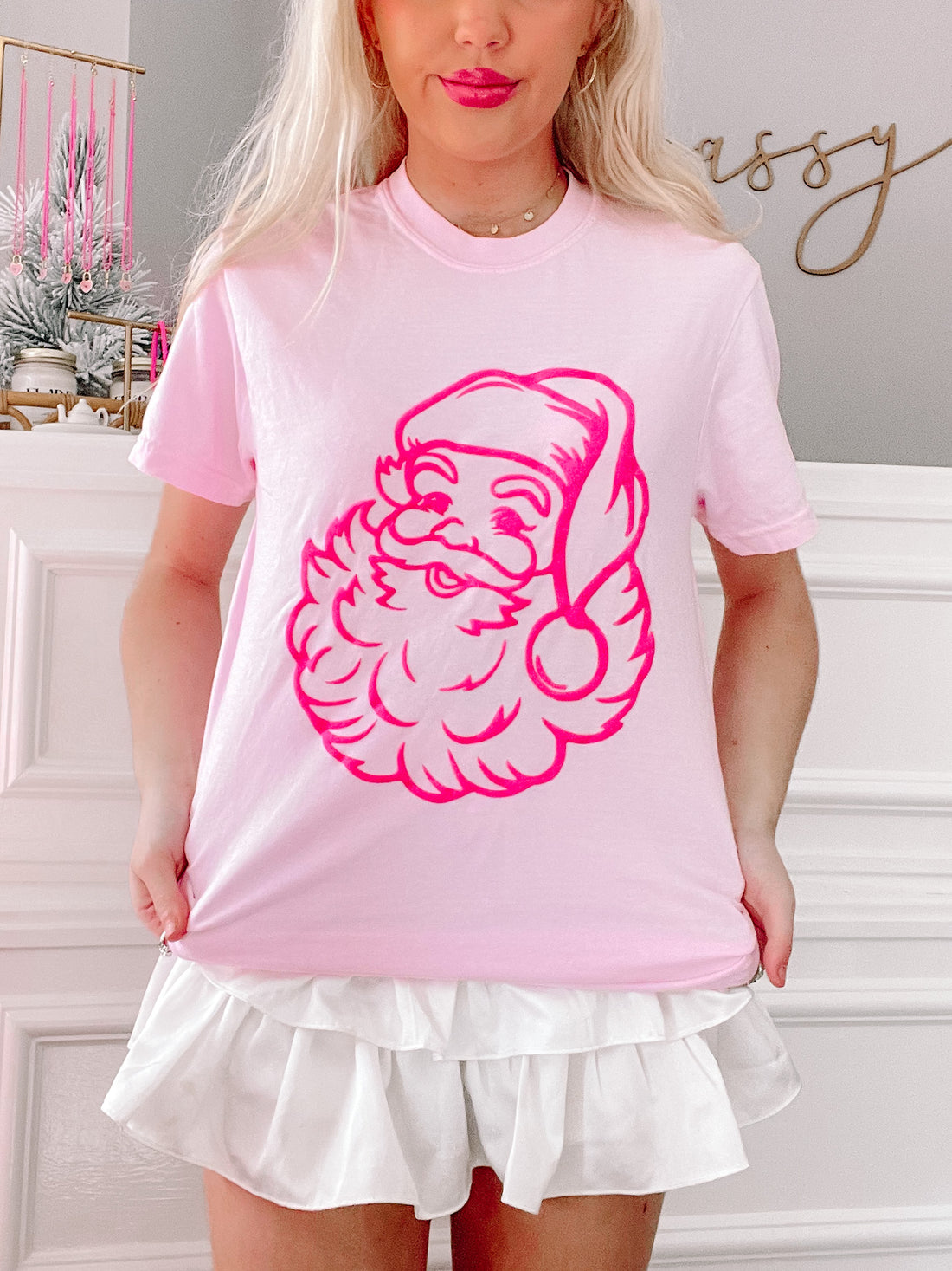 Pink t-shirt featuring a hot pink Santa graphic, modeled against a white-trimmed wall from Sassy Shortcake
