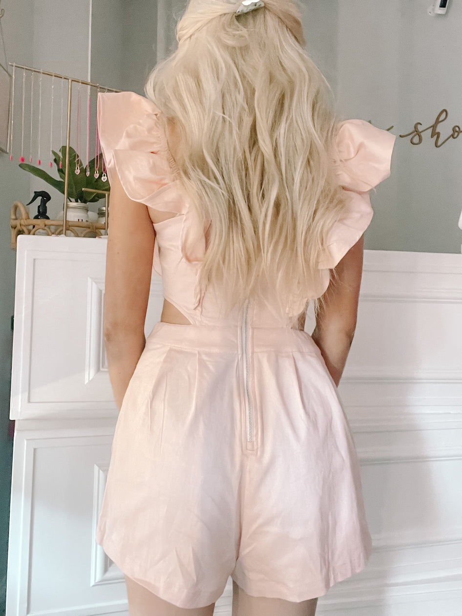 Back view of a blush-pink romper with ruffle sleeves, shown against a white background.
