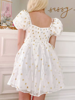 White mini dress with gold and silver star print, puff sleeves, and smocked bodice.
