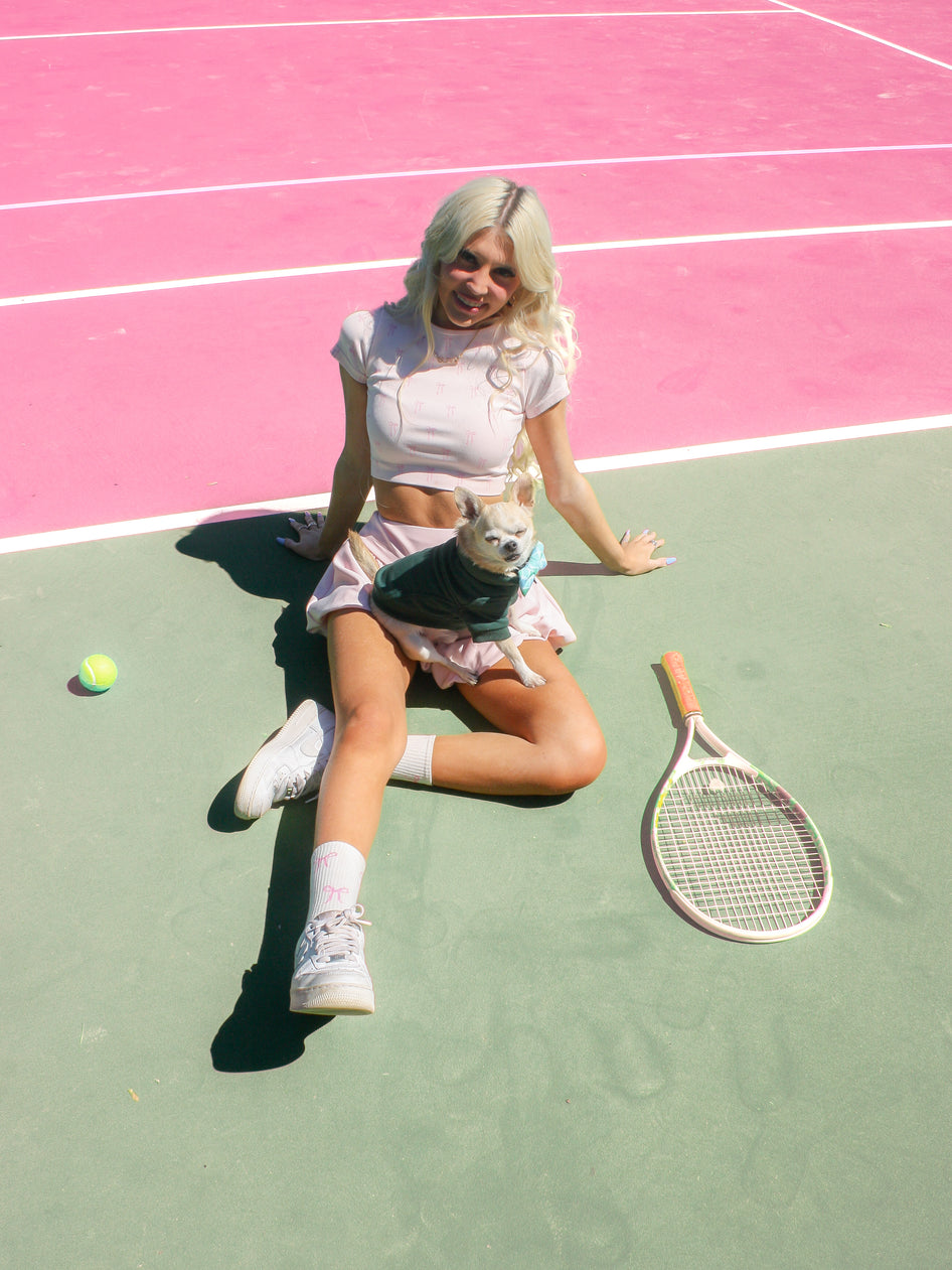 Woman relaxing on a pink tennis court with her small dog and tennis racket.

