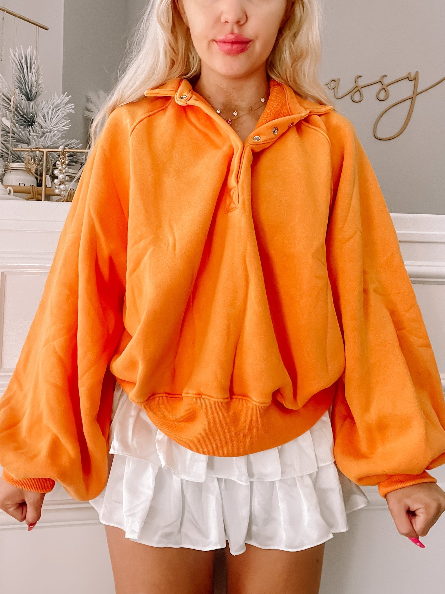 Bright orange pullover sweater with balloon sleeves, modeled with a white ruffled skirt.
