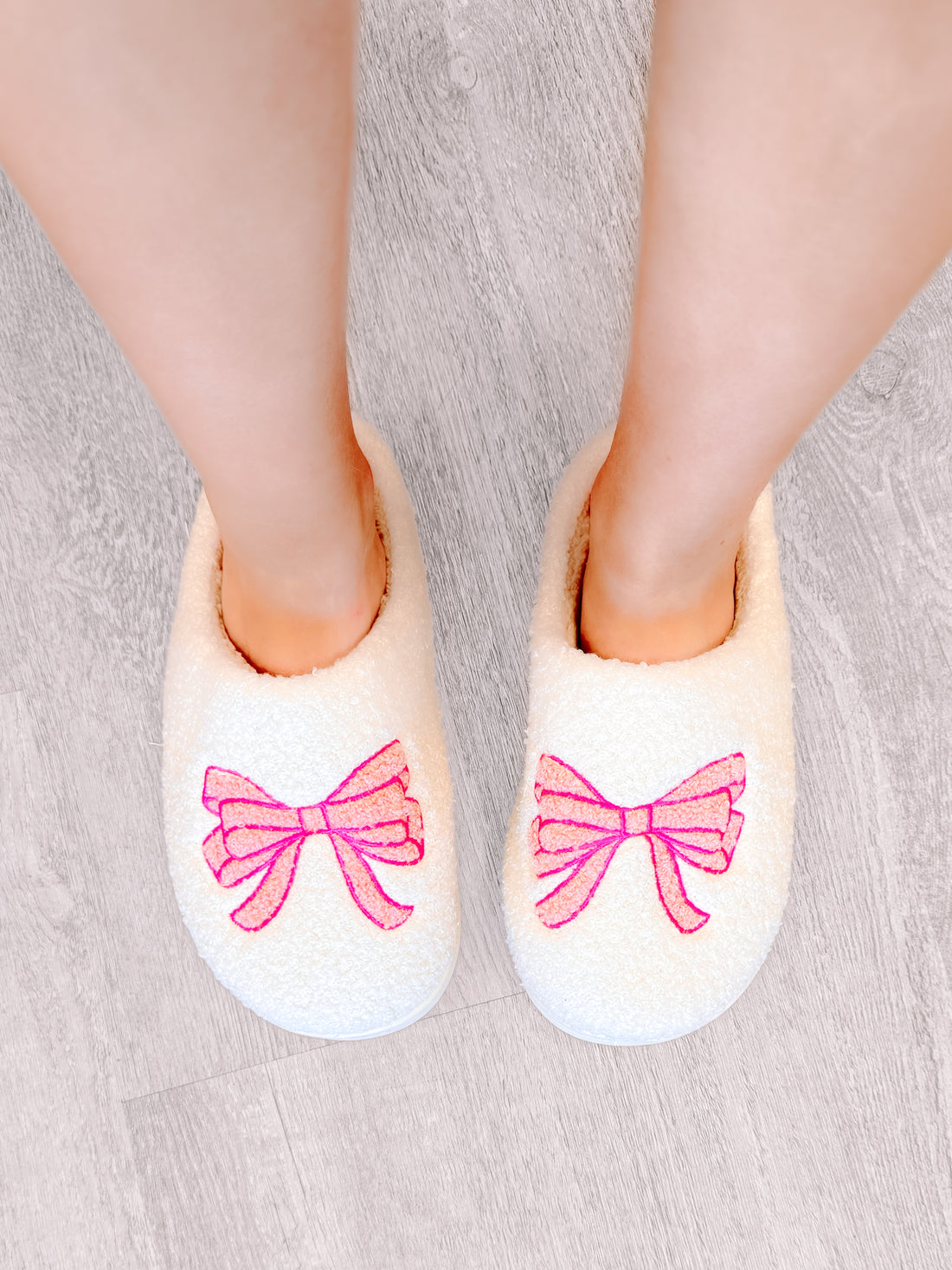 White fuzzy slippers with pink bows, cozy and comfortable footwear.
