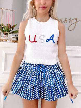 White knit cropped tank with festive USA lettering, paired with a blue star-print mini skirt.
