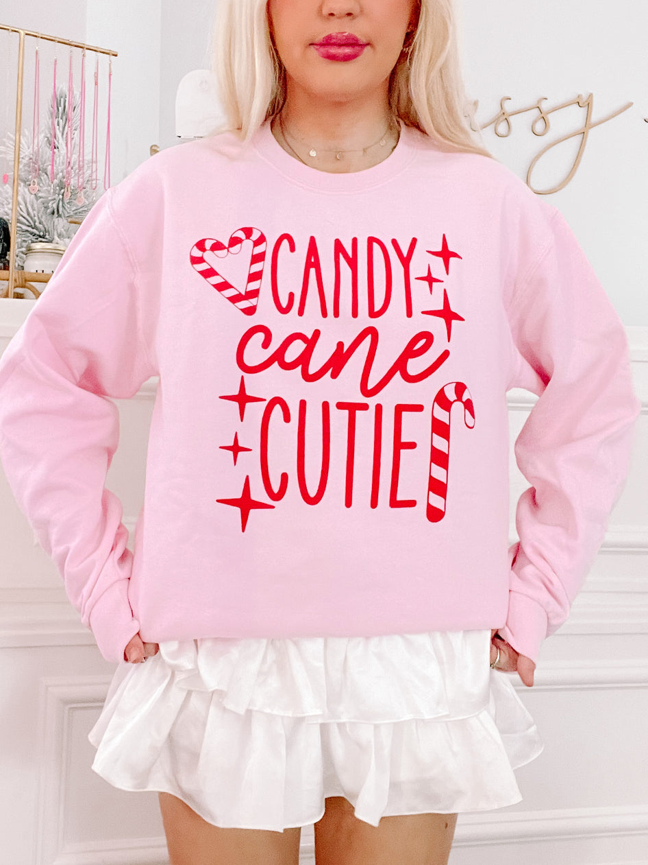 Pink crewneck sweatshirt with red candy cane design and festive text.
