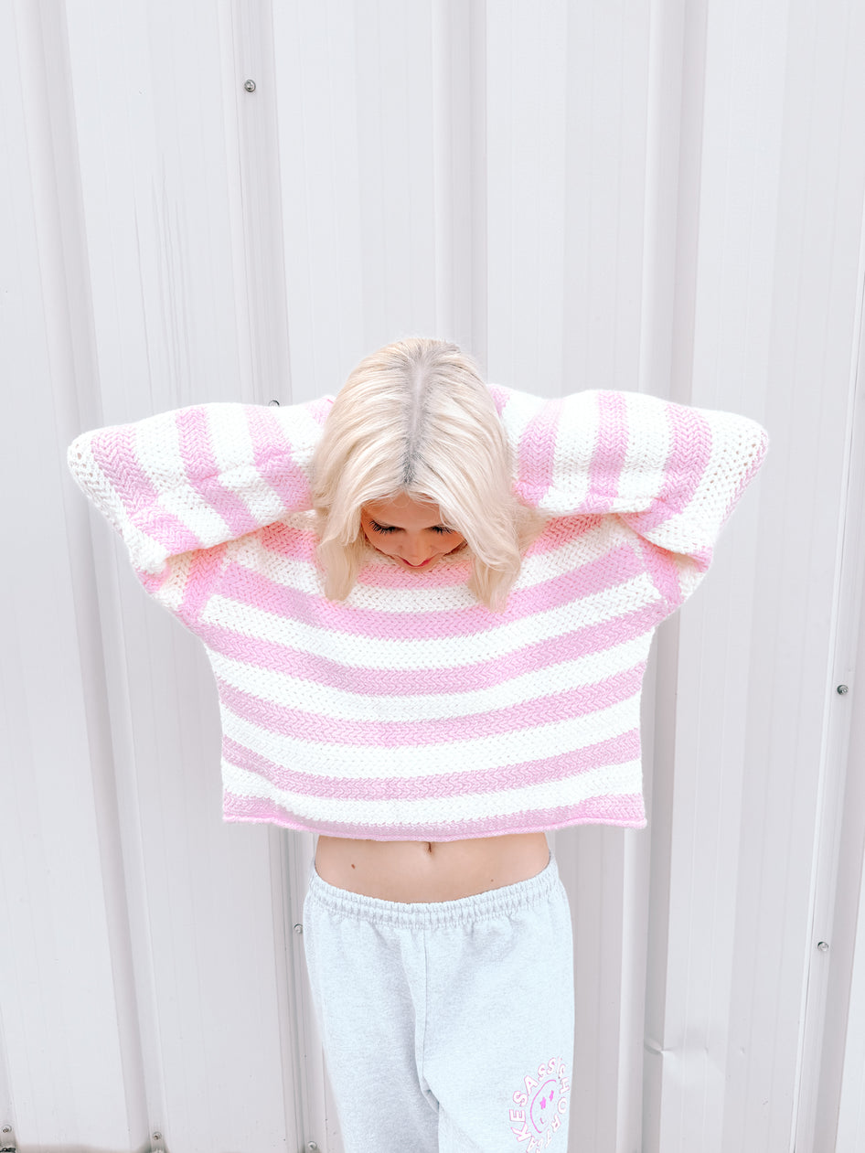 Pink and white striped cropped sweater on model against white background.
