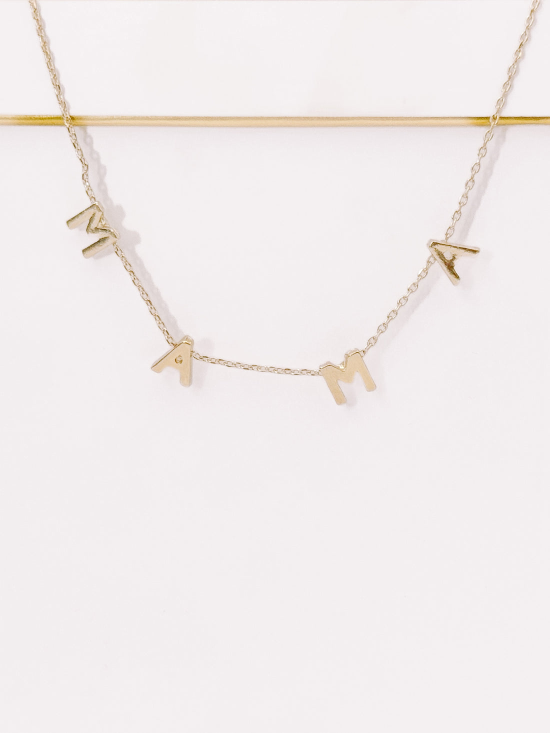 Gold "Mama" necklace on white background, delicate chain.
