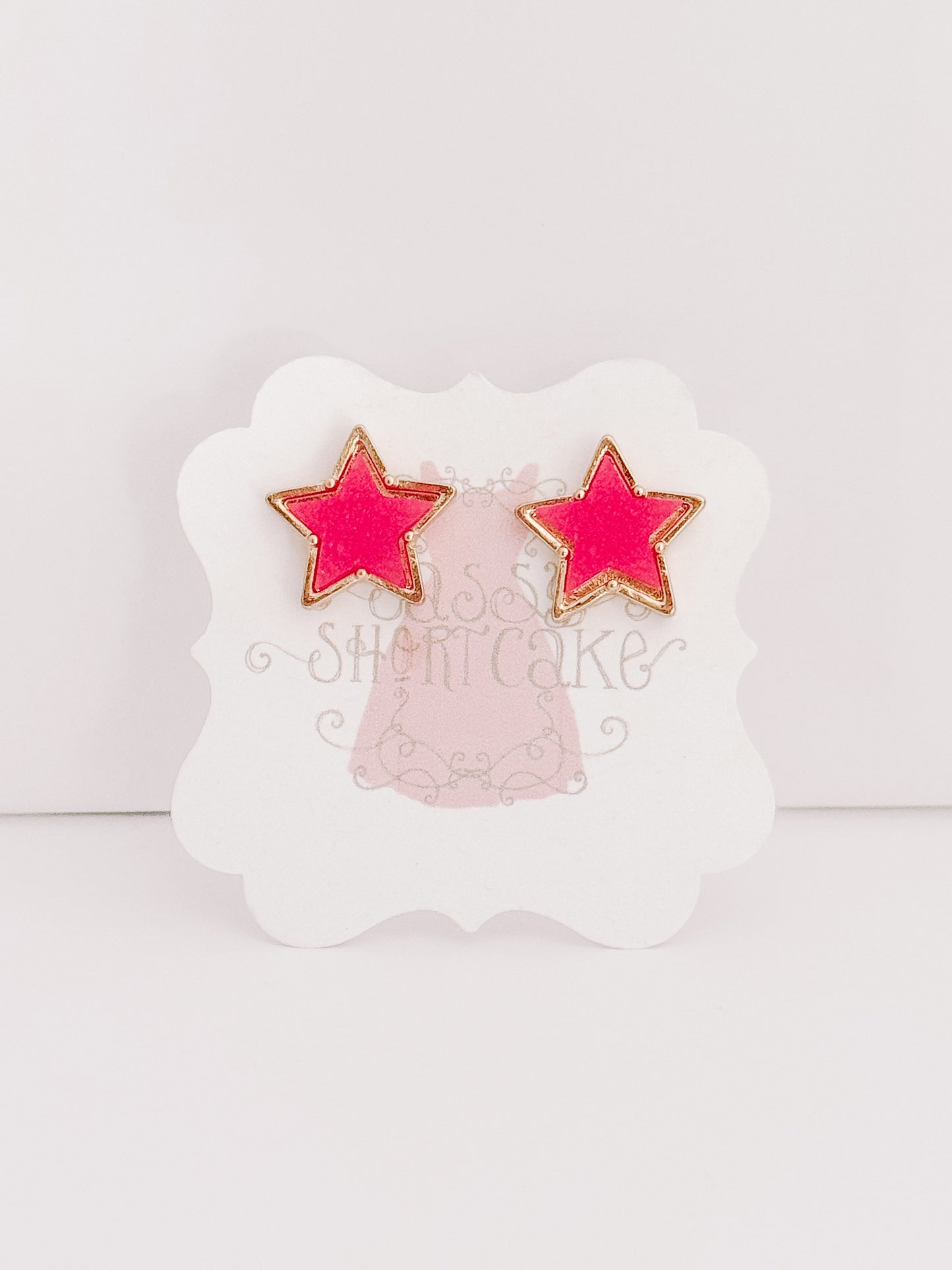 Pink star-shaped stud earrings with gold accents, displayed on a product card.
