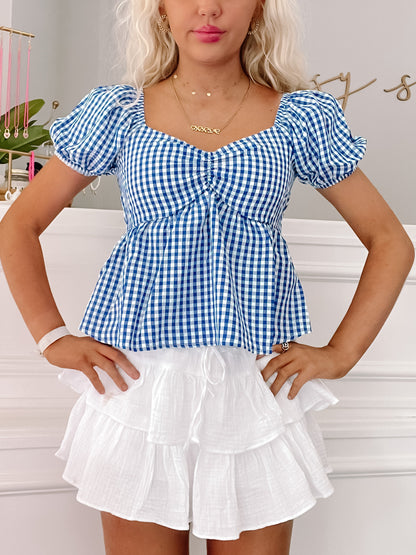 Blue gingham puff-sleeve top paired with a white tiered mini skirt.
