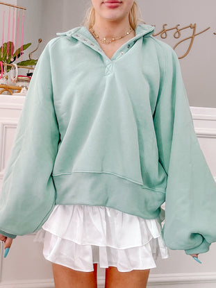 Mint green pullover sweatshirt with balloon sleeves and a buttoned henley neckline, paired with a white ruffled mini skirt.
