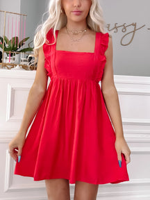 Red sleeveless mini dress with ruffles, showcased against a white wall.
