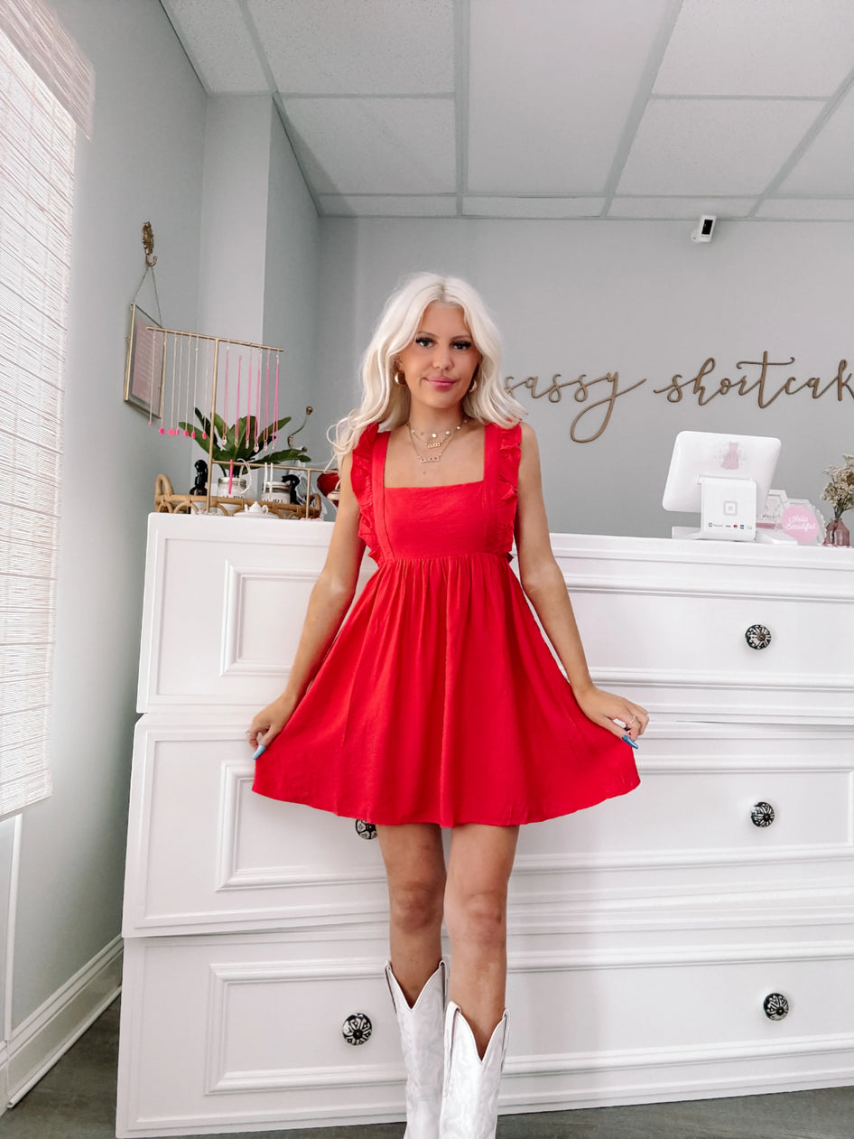 Red ruffle mini dress styled with white cowboy boots, shown in a bright room.

