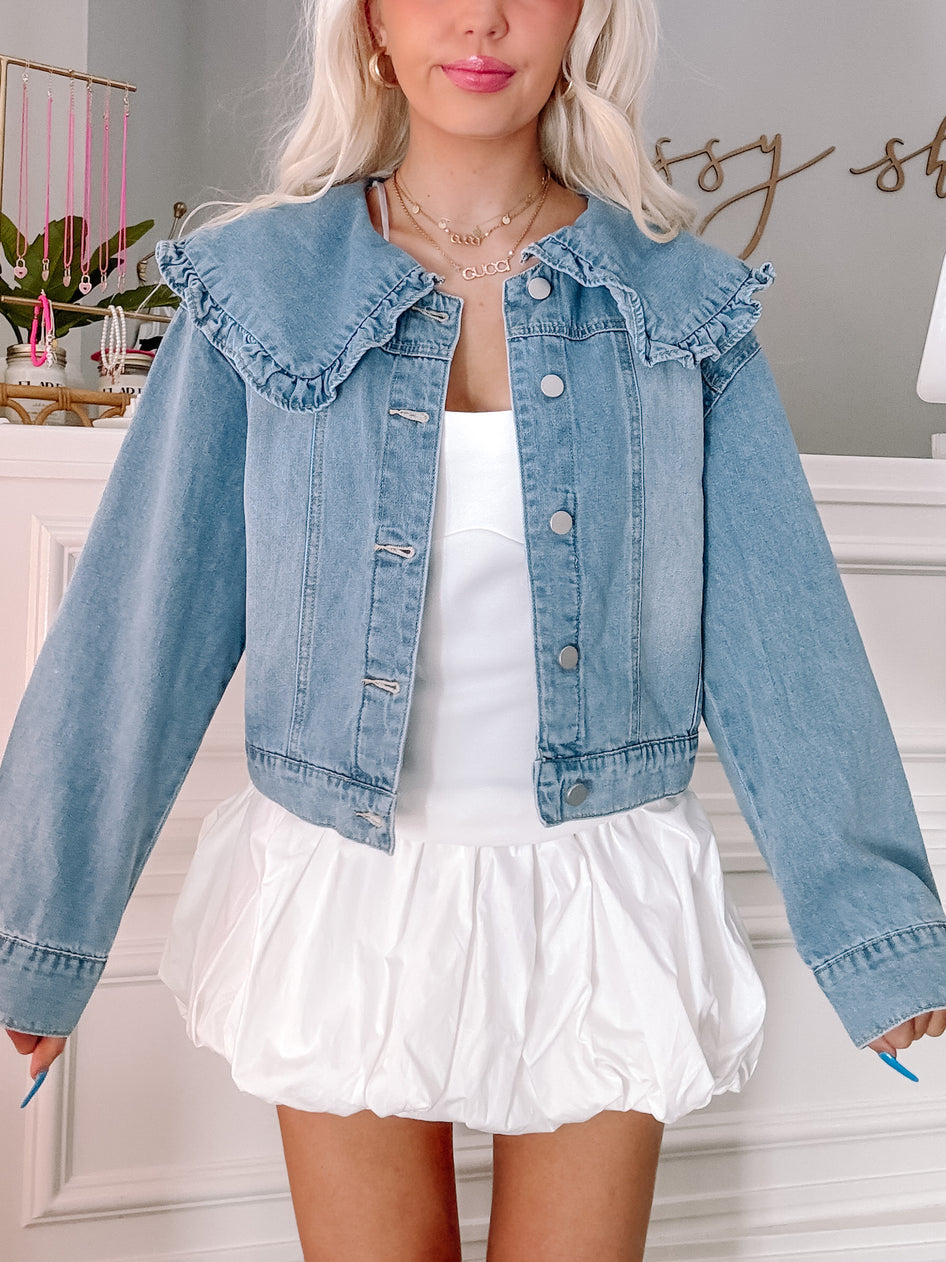Light wash denim jacket with ruffled collar paired with a white bubble skirt.

