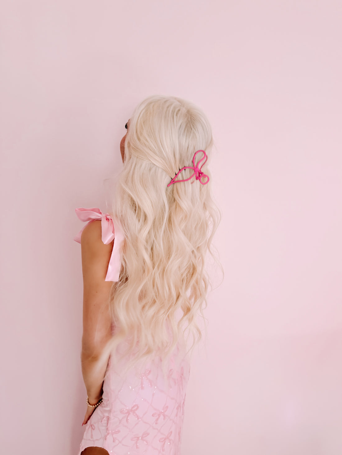 Pink bow hair clip in blonde hair against a pink background.
