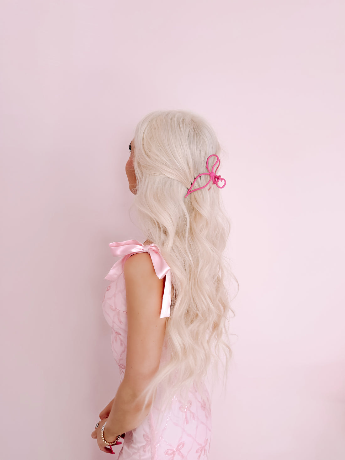 Pink claw hair clip in long blonde hair against a pink background.
