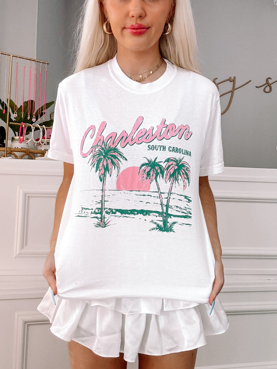 White tee featuring a palm tree and ocean scene graphic, "Charleston, South Carolina" text.
