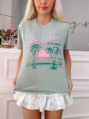 Sage green Charleston, South Carolina tee with palm tree graphic; model wearing a white ruffle skirt.
