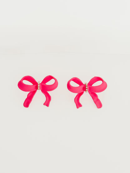 Pink bow earrings with rhinestone accents against a white background.
