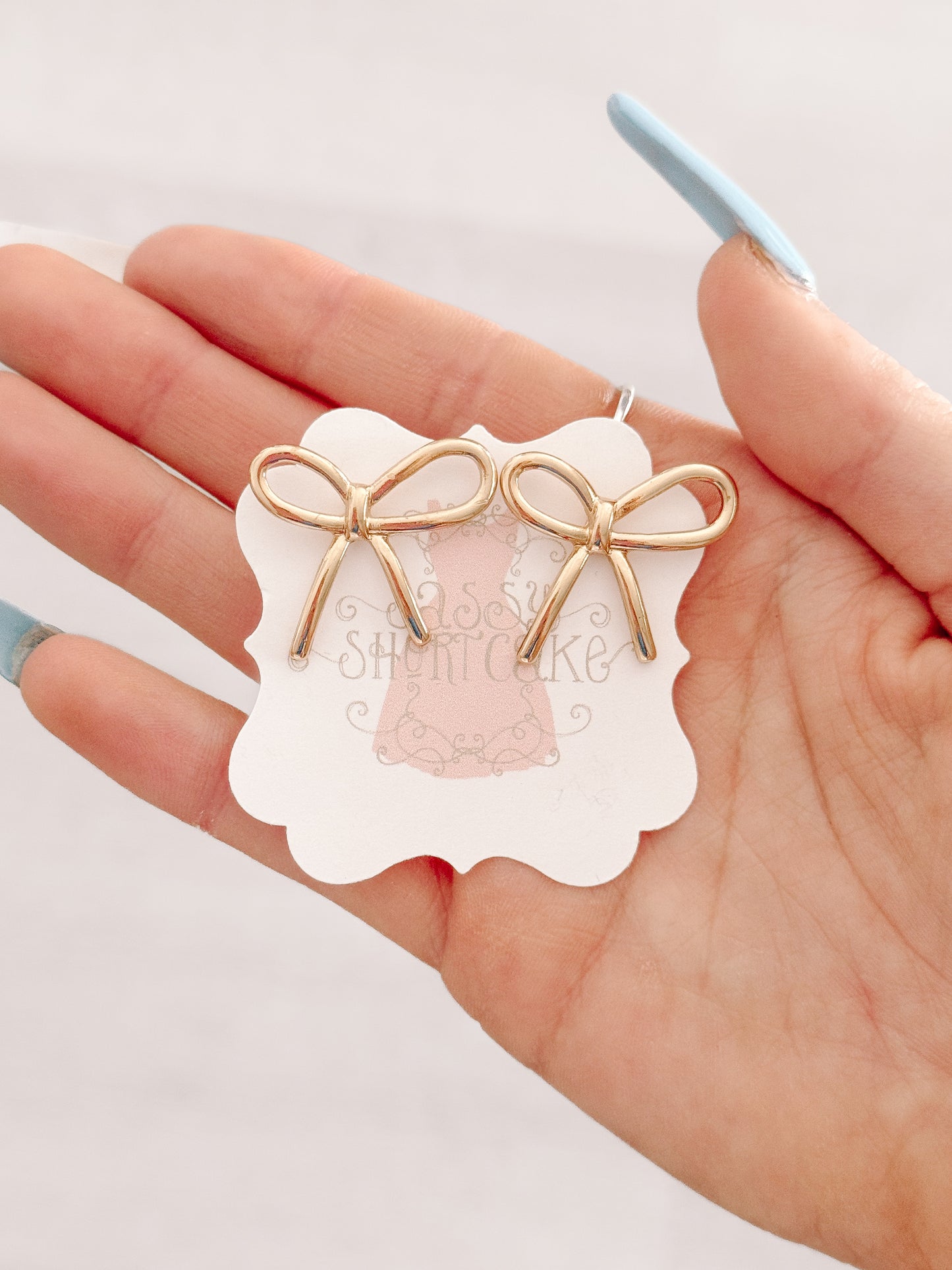 Gold bow earrings displayed on hand, delicate design.
