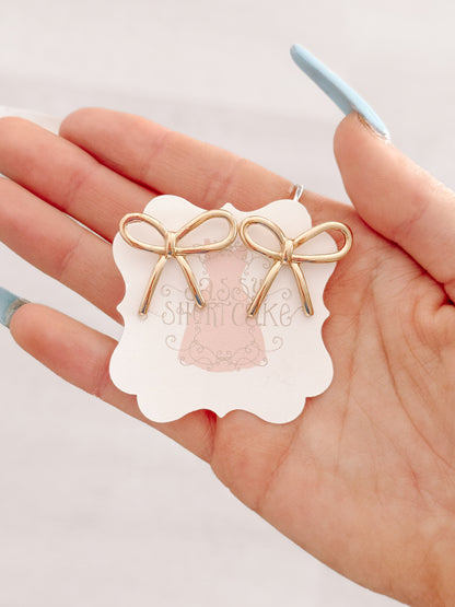 Gold bow earrings displayed on hand, delicate design.
