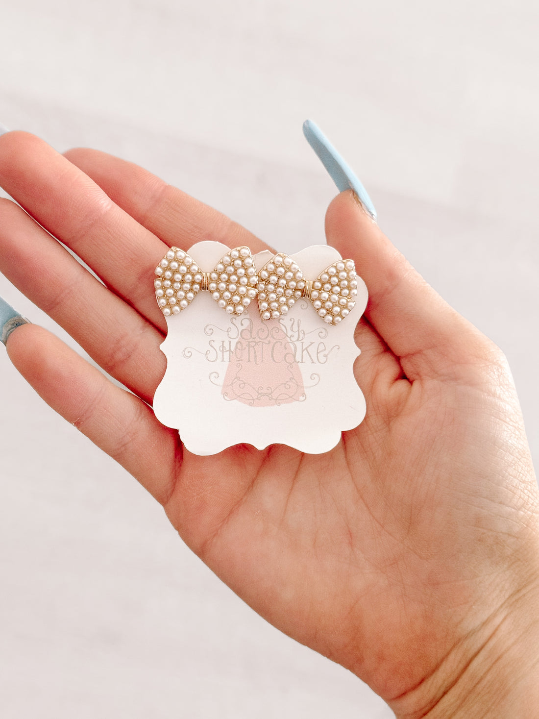 Gold bow earrings adorned with tiny white pearls, displayed on hand.
