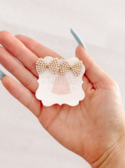 Gold bow earrings adorned with tiny white pearls, displayed on hand.
