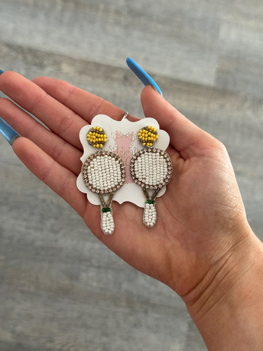 Beaded tennis racquet earrings displayed on hand, featuring white and yellow accents.
