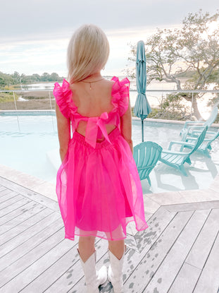 Hot pink mini dress with ruffle sleeves, bow back detail, worn poolside.
