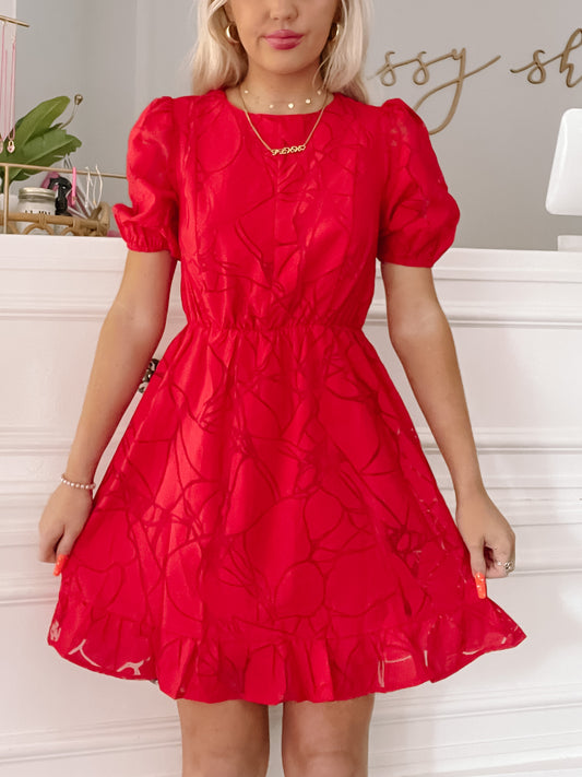 Red short-sleeved mini dress with an abstract print, cinched waist, and ruffled hem.