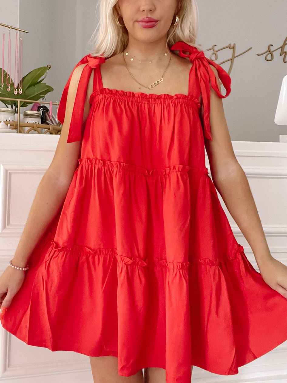 Red tiered mini dress with shoulder ties, styled for a casual look.
