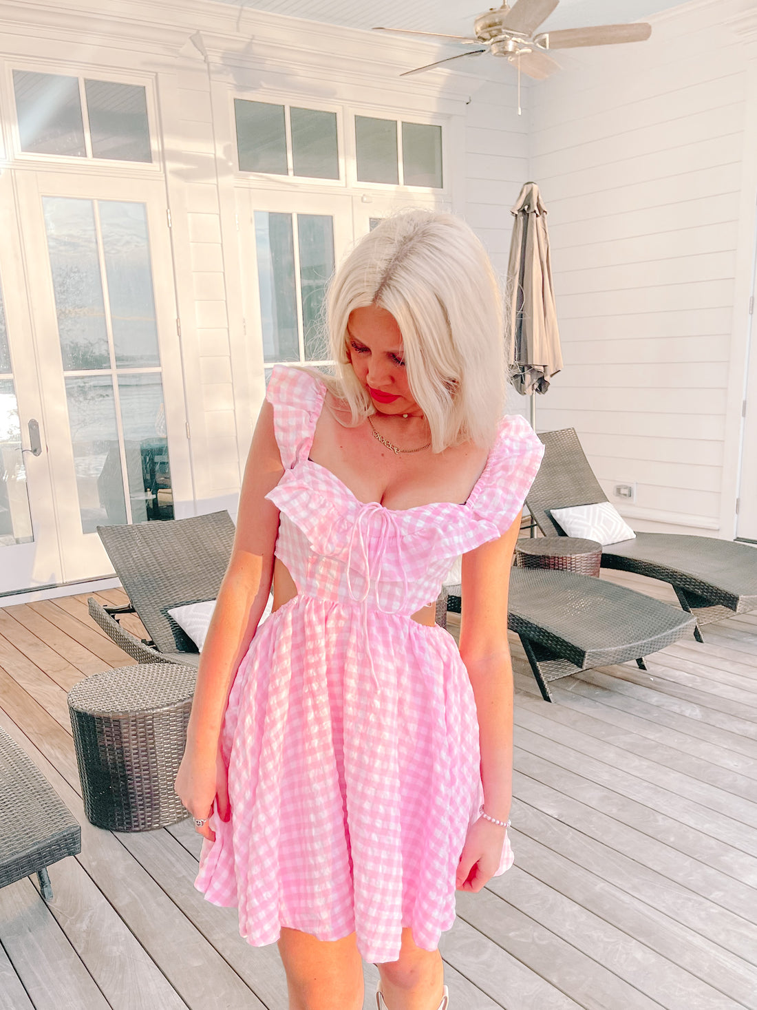 Pink gingham dress with ruffles, modeled outdoors on a patio.
