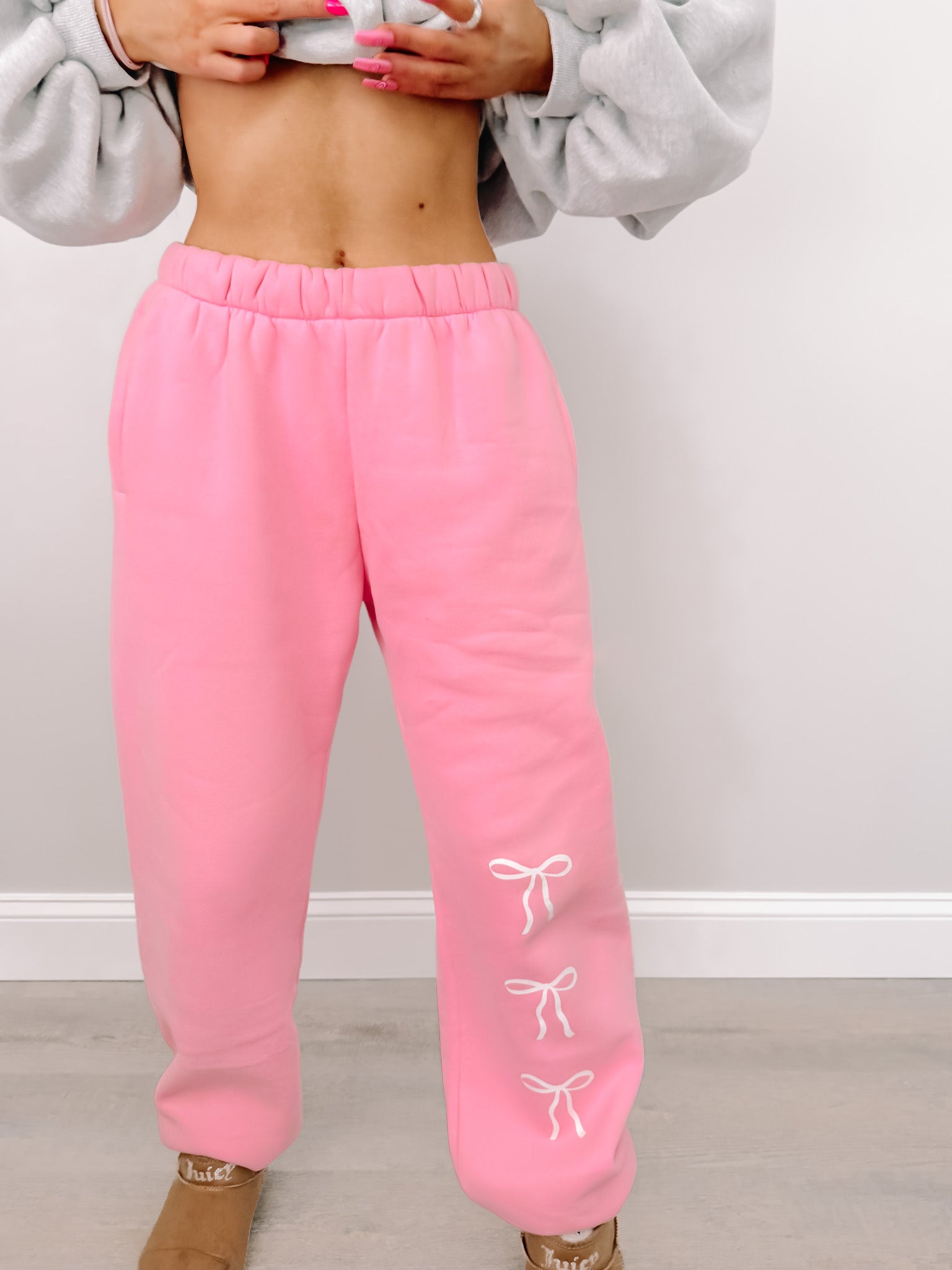 Pink sweatpants with cute white bow details, shown on a model against a light background.
