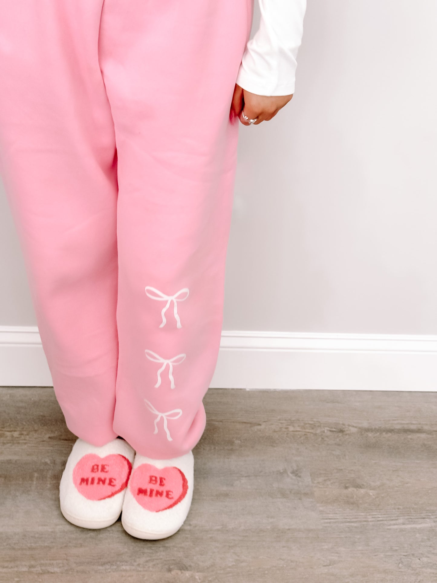 Pink sweatpants with cute bow details, paired with "Be Mine" slippers; a cozy Valentine's Day look.
