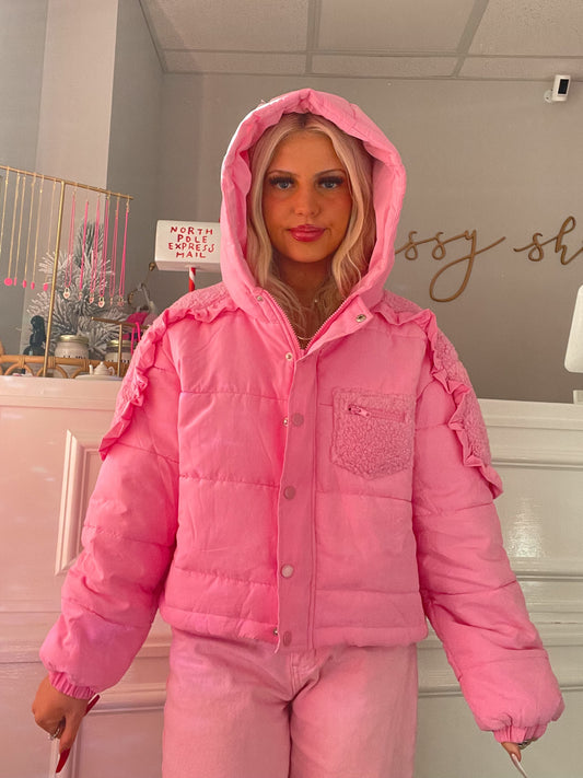 Pink puffer jacket with ruffled sleeves, shown on a model in a boutique setting.