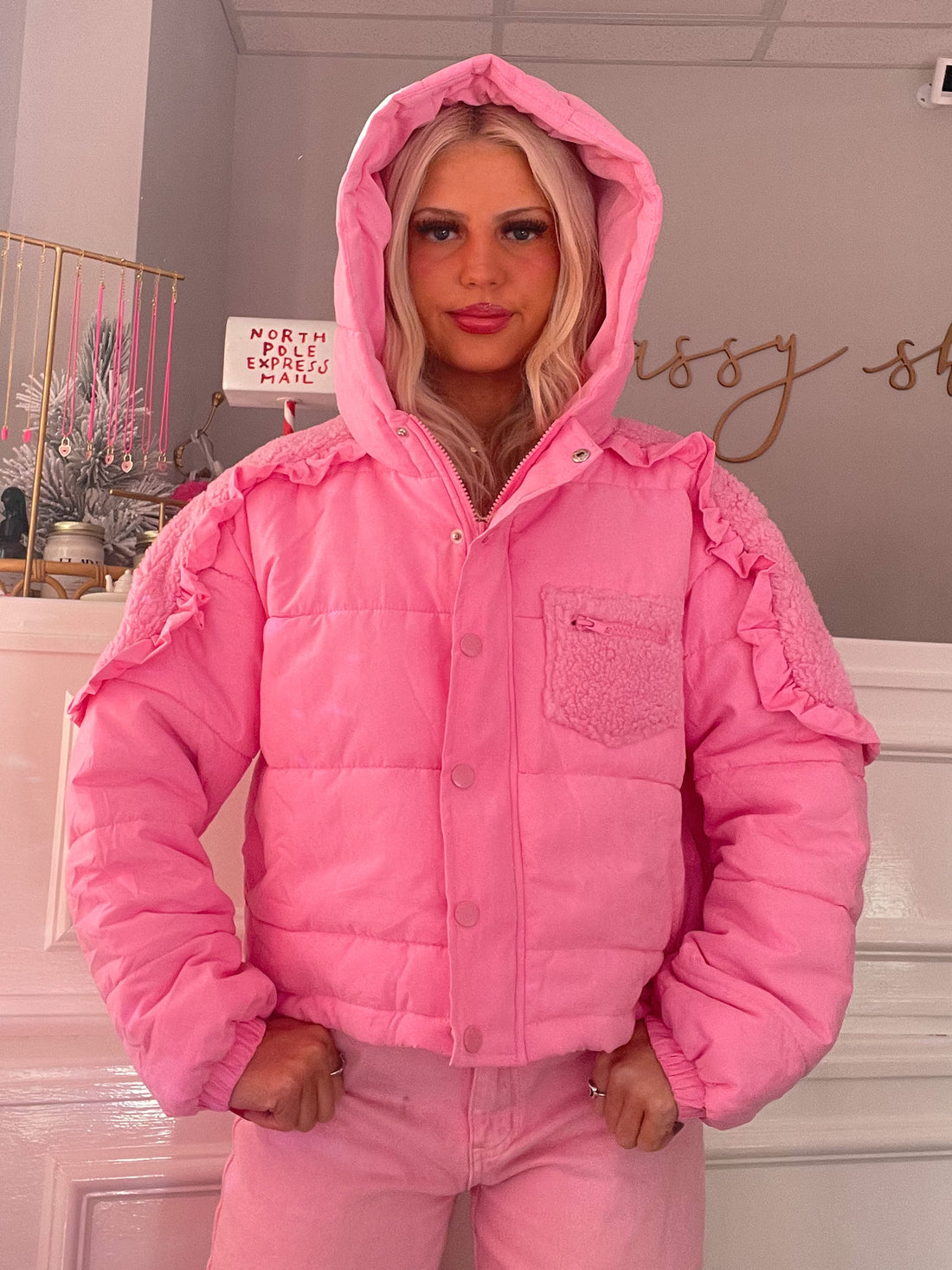Pink puffer jacket with ruffled sleeves and sherpa-lined hood, showcased on a model.
