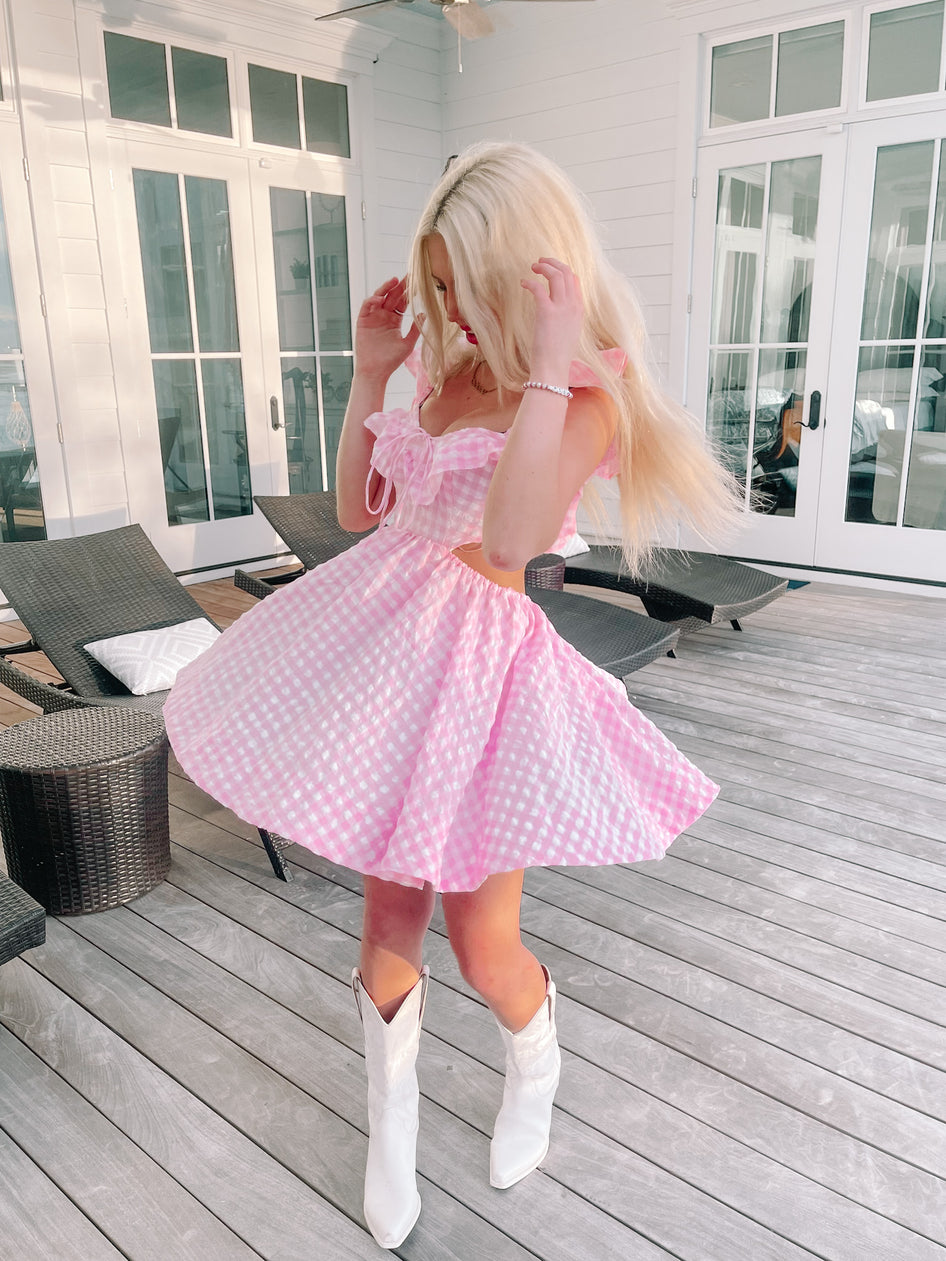 Pink gingham dress twirled outdoors on a wood deck.
