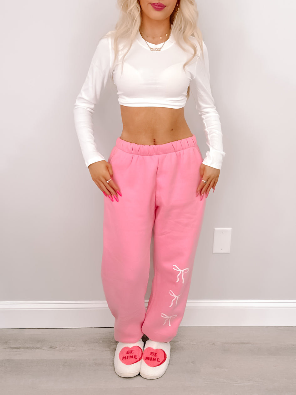 Pink sweatpants with bow details, styled with a white cropped top.

