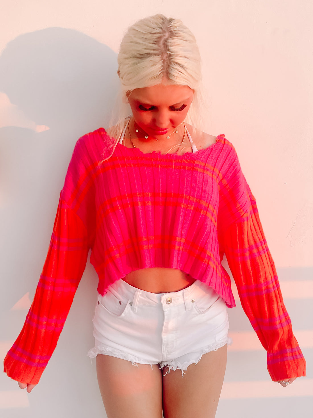 Hot pink cropped sweater with orange stripes, styled with white denim shorts.
