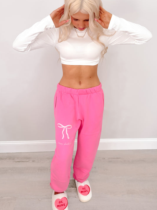 Pink sweatpants with bow detail, worn with heart slippers; lifestyle shot.