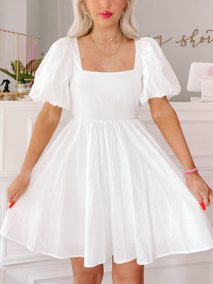 White puff-sleeve mini dress, square neckline, A-line silhouette, showcased in a bright, airy room.
