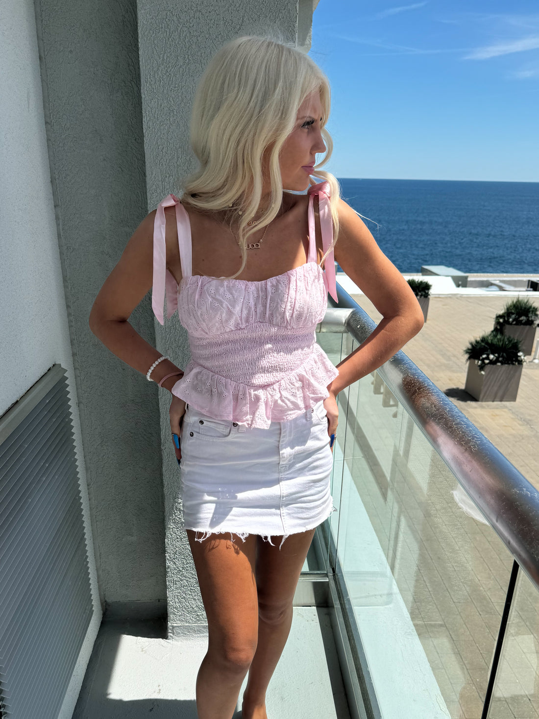 Pink eyelet crop top with satin ties, worn outdoors on a sunny day.
