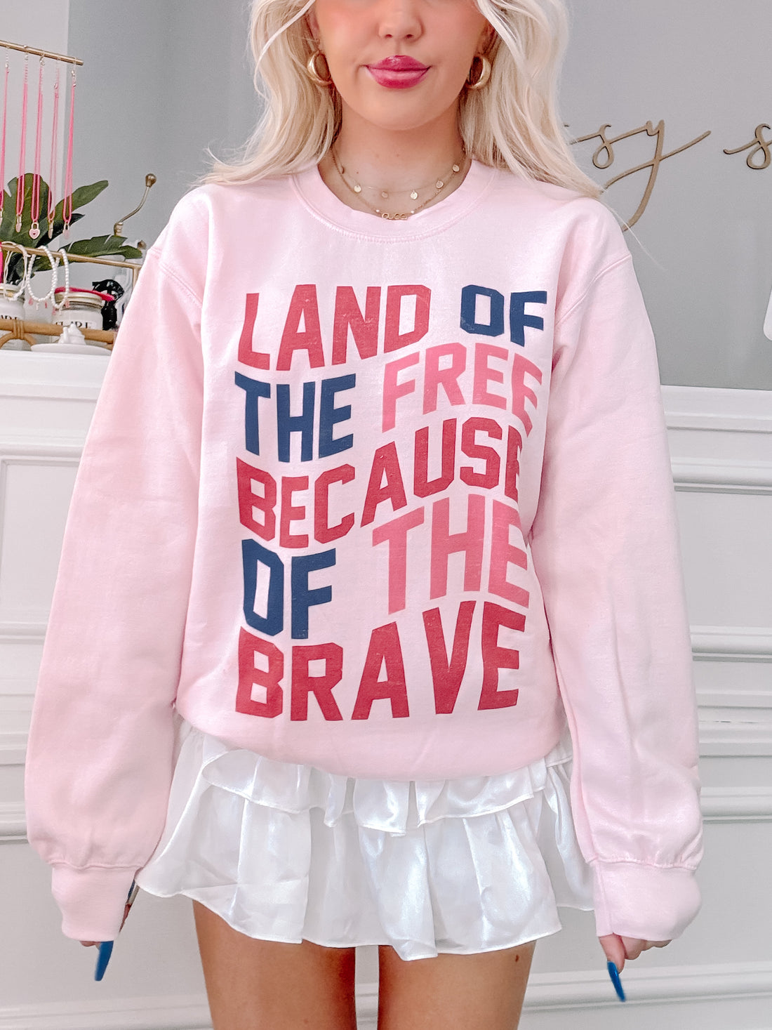 Pink crewneck sweatshirt with a patriotic message, styled with a white ruffled skirt.
