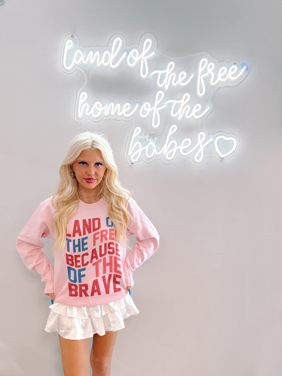 Pink crewneck sweatshirt styled with white ruffled skirt, shown against a neon sign.
