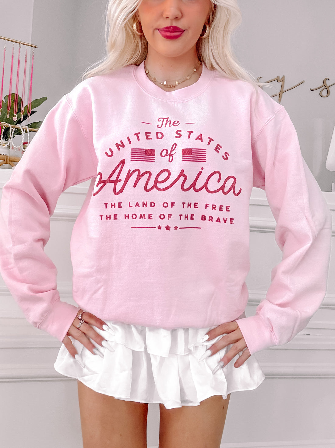 Pink crewneck sweatshirt featuring a patriotic graphic, modeled against a light background.
