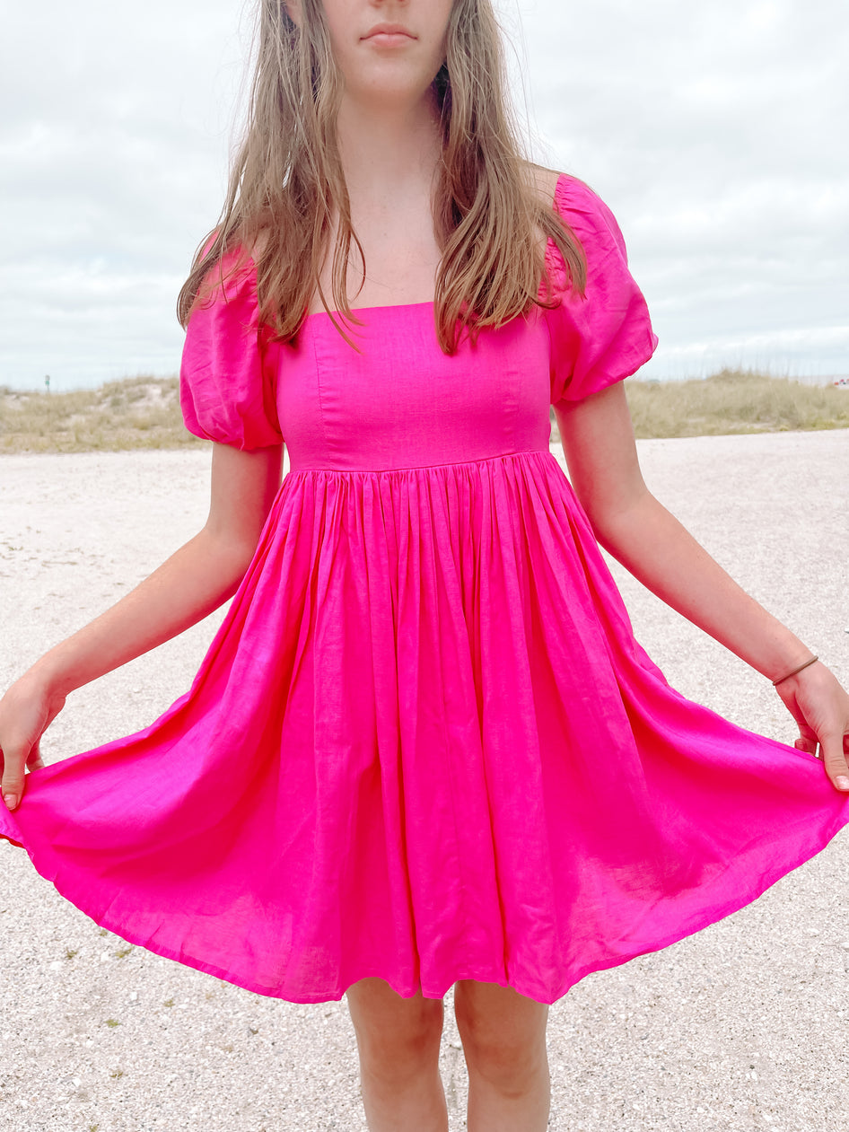 Hot pink mini dress with puff sleeves, shown outdoors on a bright day.
