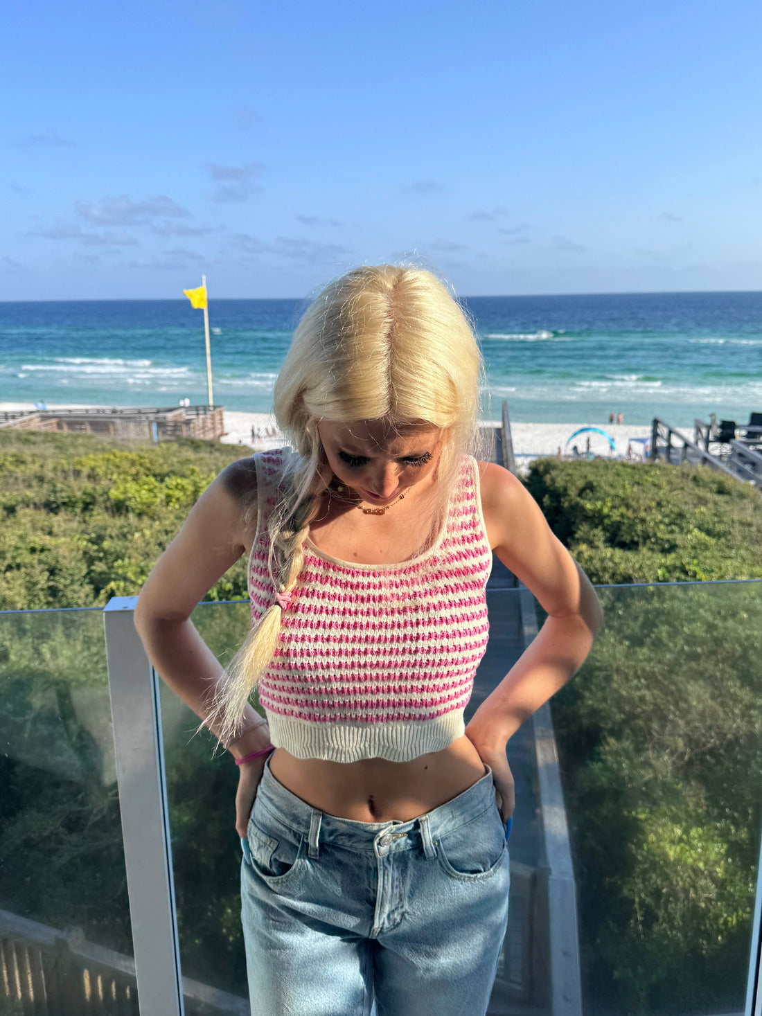 Woman in pink and white striped cropped tank top on balcony overlooking ocean.
