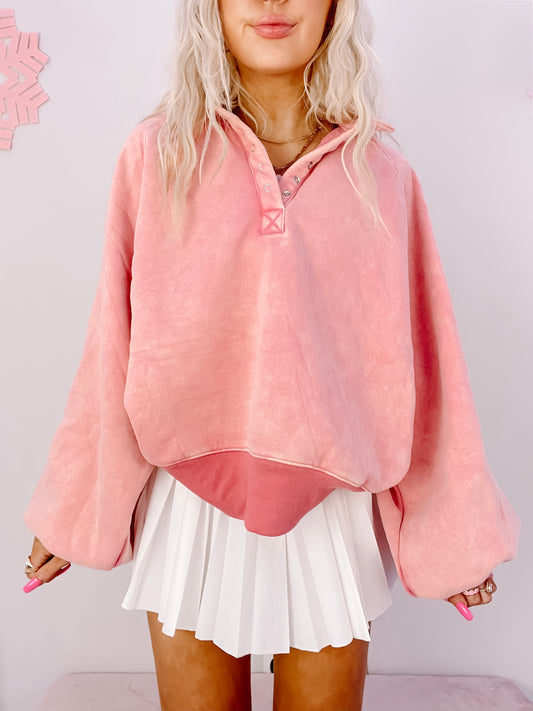 Pink button-up pullover sweater styled with a white pleated tennis skirt.
