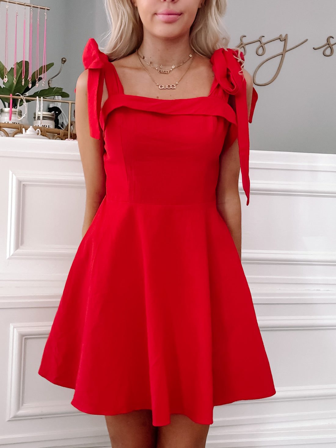 Red fit-and-flare dress with shoulder ties, shown on a model against a white wall.
