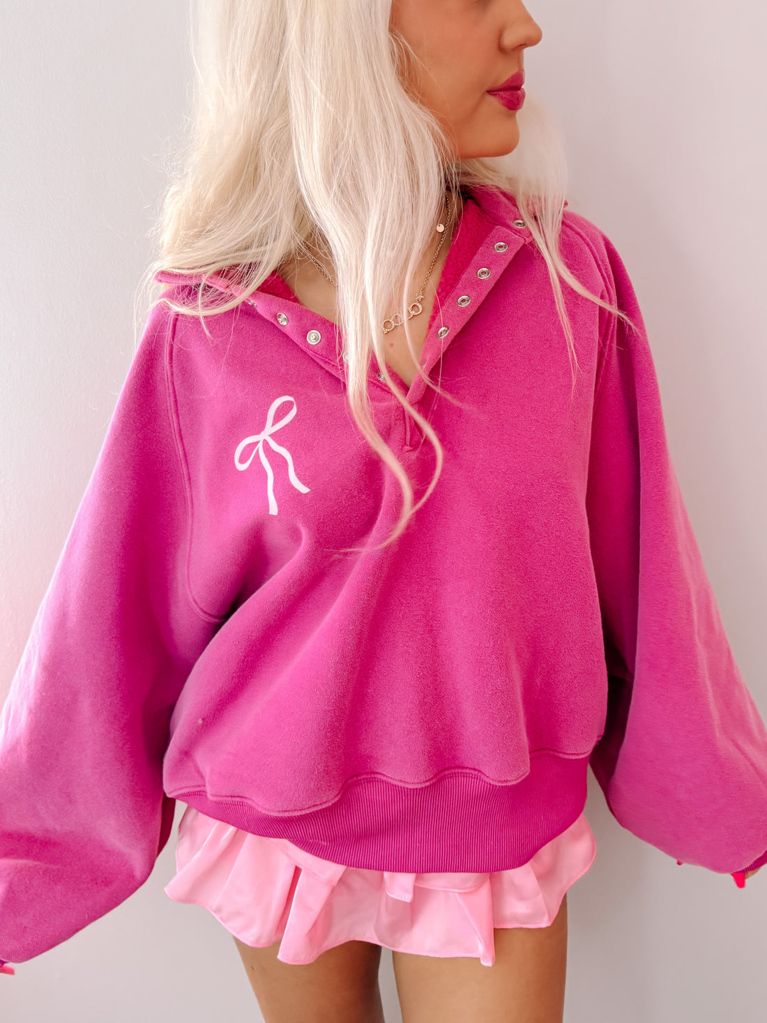 Pink pullover sweatshirt with a bow detail, shown on a model.
