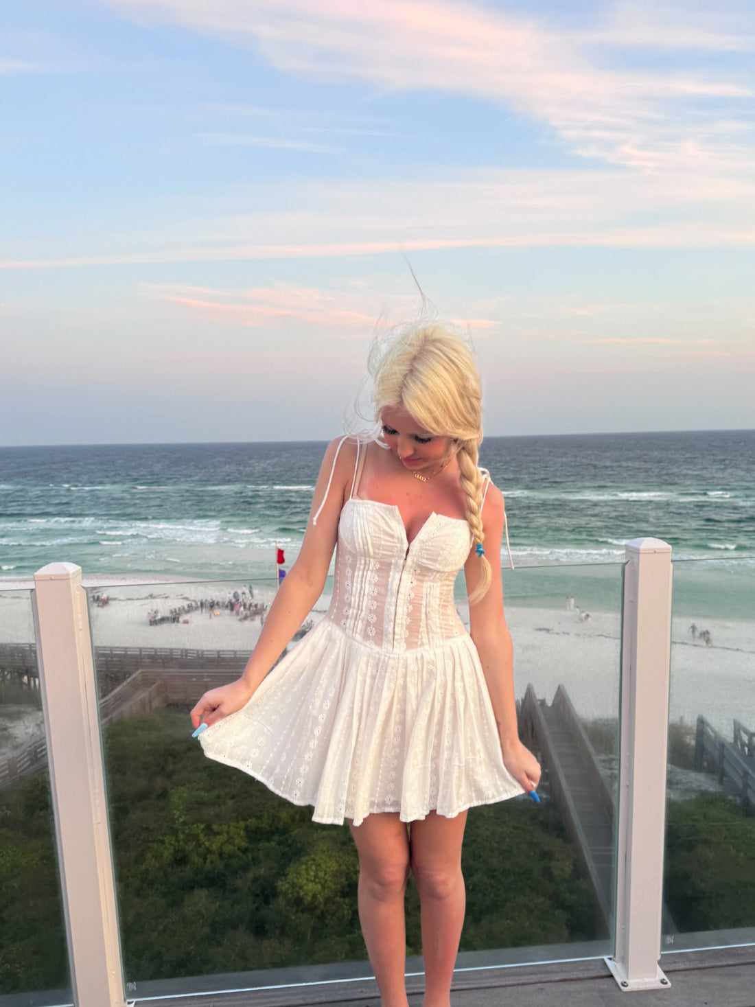 White eyelet mini dress on a beach balcony at sunset.
